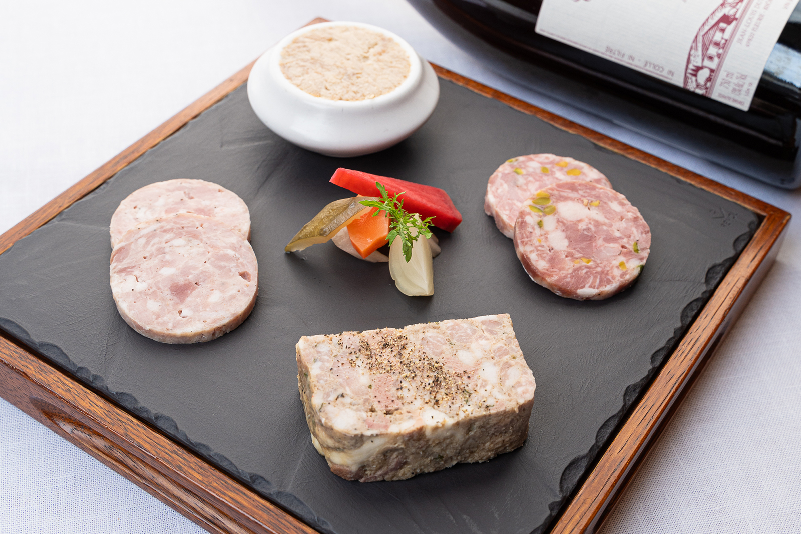 L'assiette de cochonnailles lyonnaises. Cette entrée comprend un pâté ainsi qu'un petit ramequin de rillettes, un saucisson aux pistaches et des tranches de saucisson cuit, le tout accompagné de quelques pickles.
