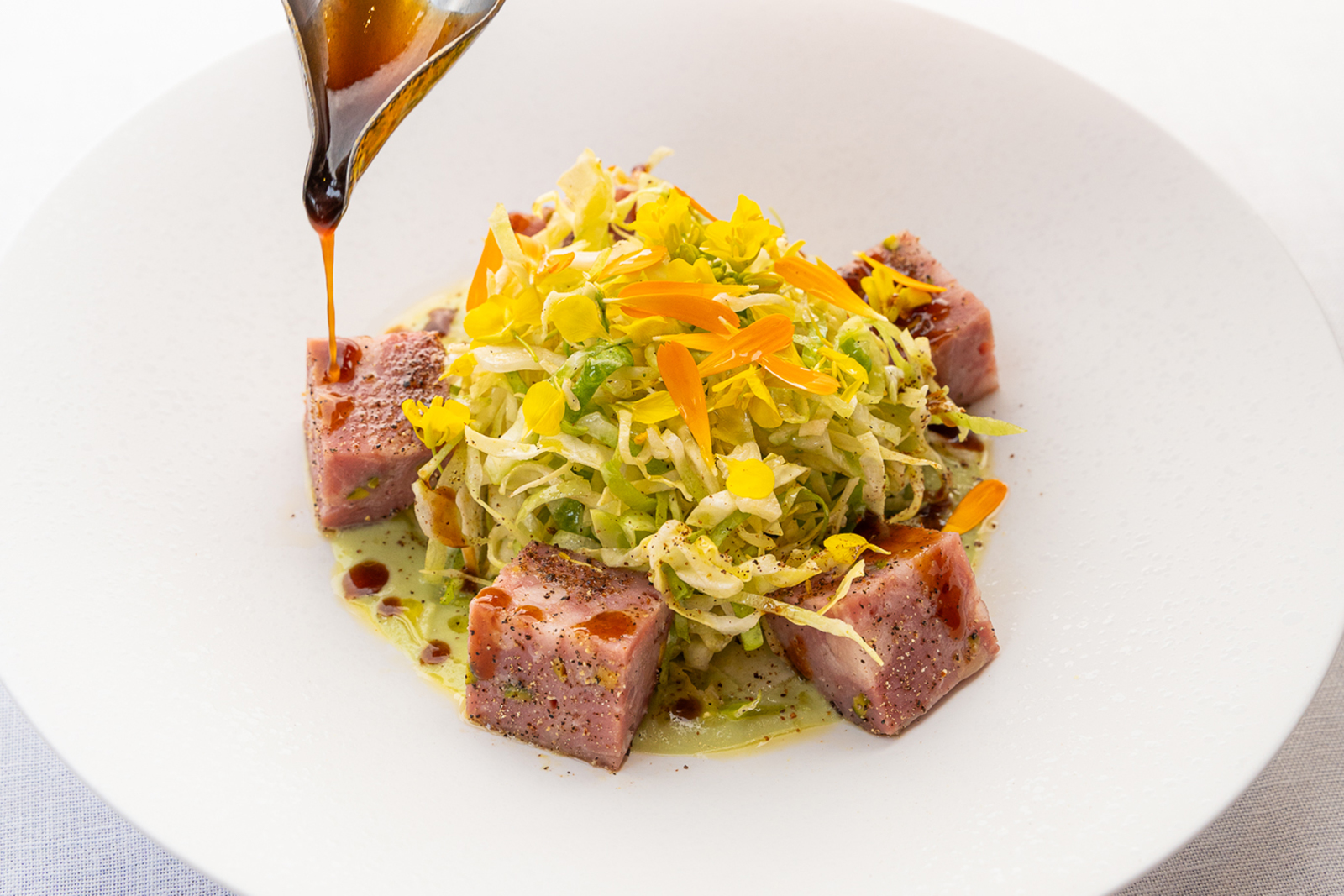 Le saucisson lyonnais pistaché servi tiède avec une salade de choux de printemps et un léger parfum de genièvre. Une réduction de jus de cochon est versée sur l'entrée avant d'être servie.