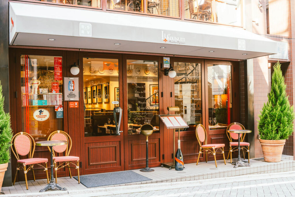 L'entrée du restaurant Lugdunum Bouchon Lyonnais à Kagurazaka, Tokyo. L'image montre la terrasse de l'établissement ainsi que les vitres à travers lesquelles on peut entrevoir l'intérieur du restaurant.